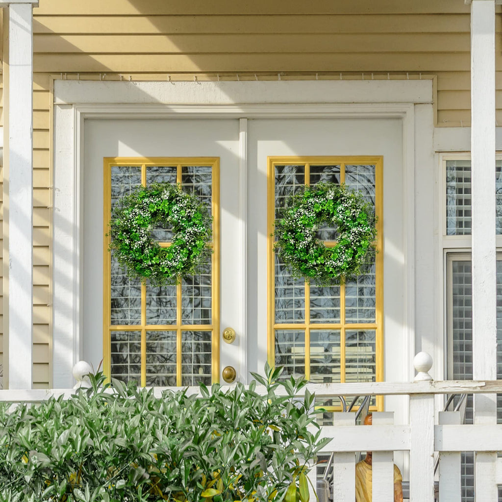 Two green shamrock wreaths with white flowers hang on a double door with yellow window frames.