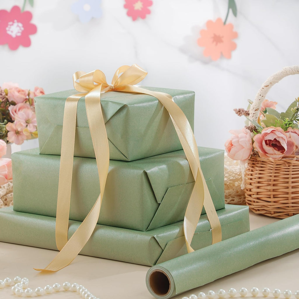 Stack of three sage green wrapped gifts tied with gold ribbon, with a roll of wrapping paper and floral decorations.