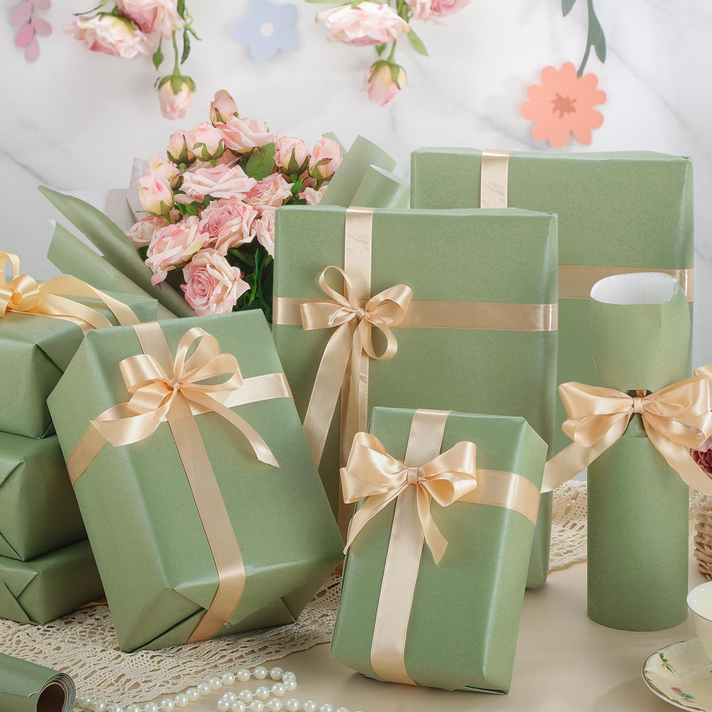 Several gift-wrapped boxes in sage green with champagne ribbon bows, arranged with a bouquet of pink roses and decorative paper flowers.