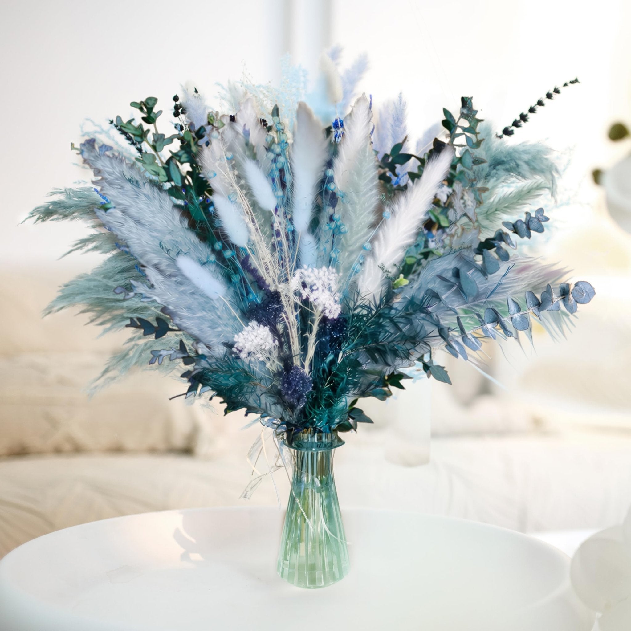 Dusty blue dried pampas grass bouquet with white grass, reeds, eucalyptus, bunny tail, and lavender in a green vase.