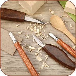 Wood carving tools and wood shavings on a wooden surface, including knives and a spoon blank.