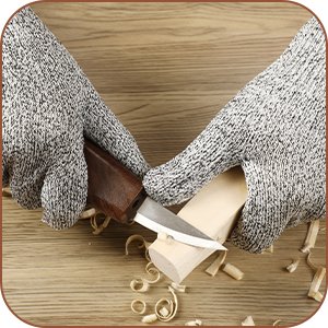 Hands wearing protective gloves carving a piece of wood with a knife, creating wood shavings.