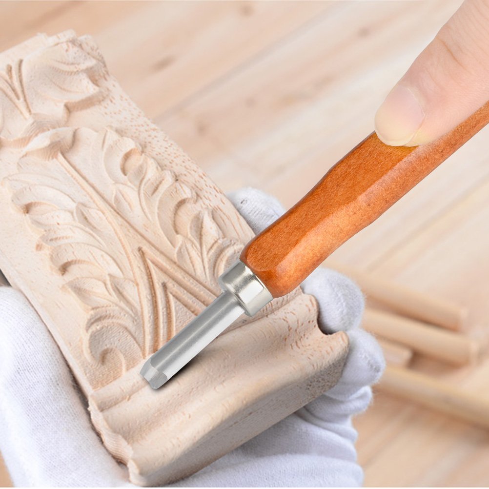 Close-up of a gloved hand using a wood carving tool to carve intricate details into a piece of wood.