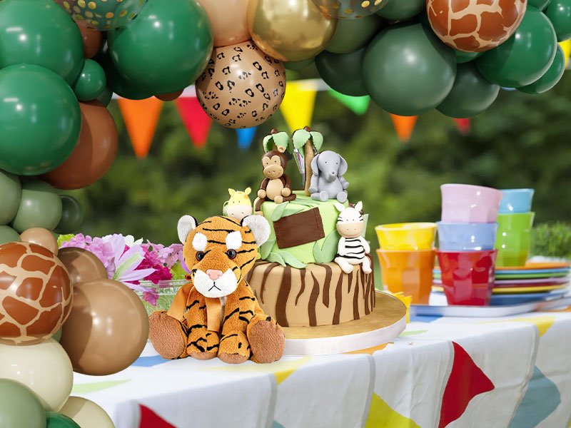 Jungle safari themed birthday cake with animal figurines and balloons, set on a table with colorful cups and plates.