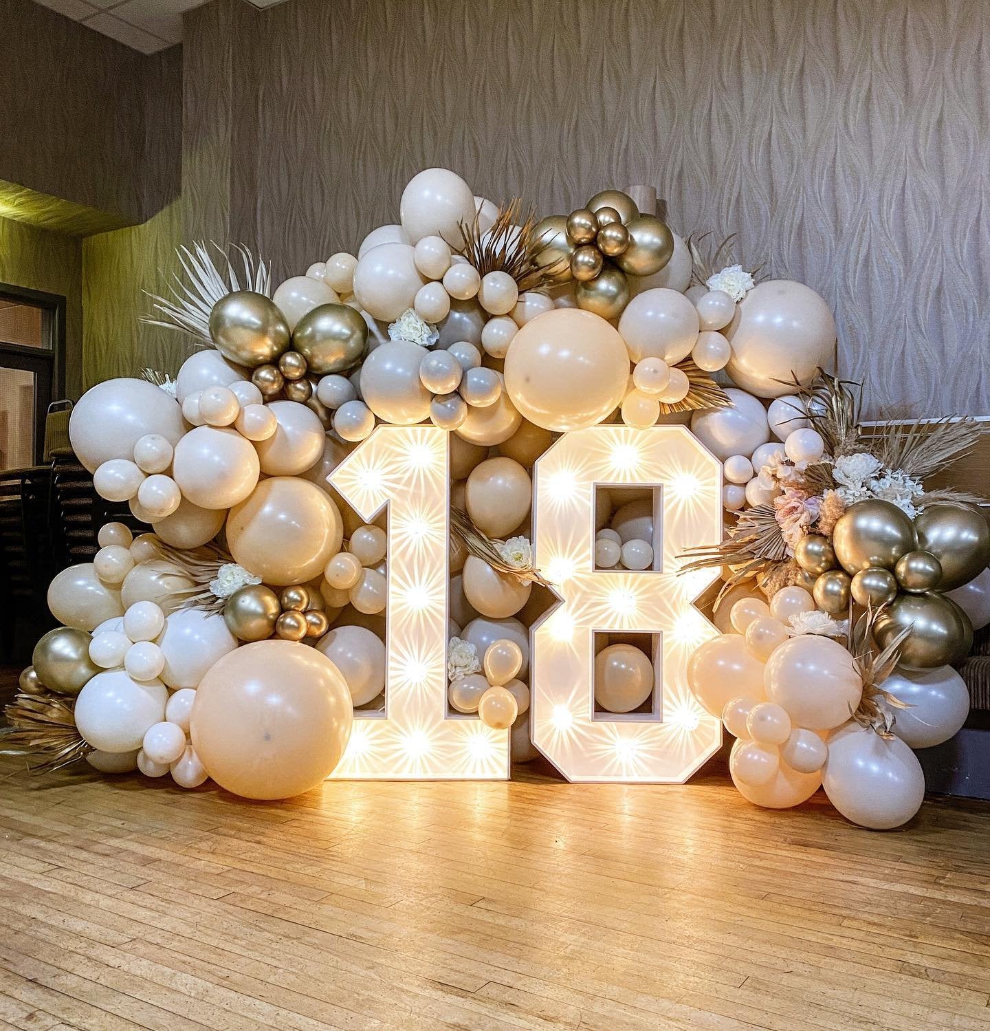 Large light-up numbers 1 and 8 decorated with a balloon arch in sand, white, and gold colors.