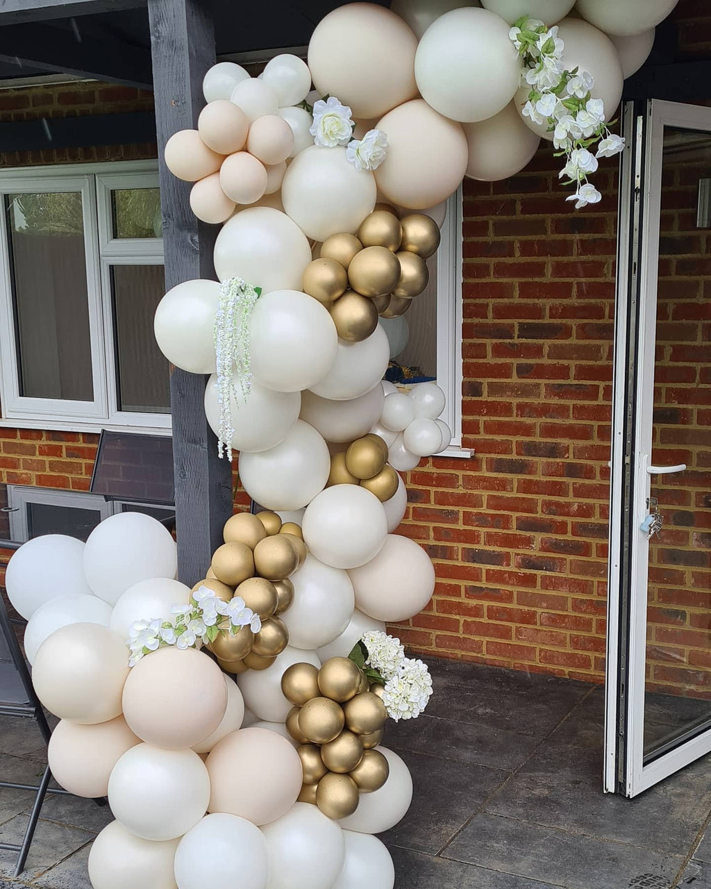 Sand white and gold balloon arch with white flowers draped over a doorway