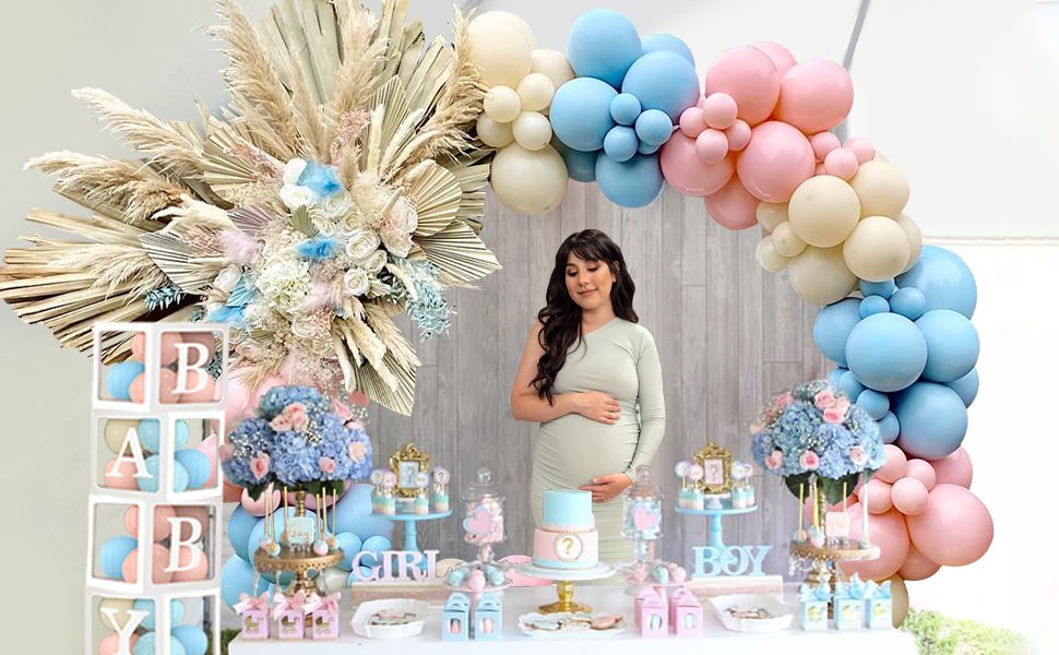 Pregnant woman at a gender reveal party with pink and blue balloon arch, baby blocks, and dessert table