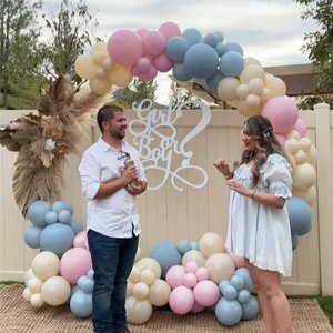 Couple celebrating at a gender reveal party with pink, blue, and cream balloon arch and 'Girl or Boy?' sign.