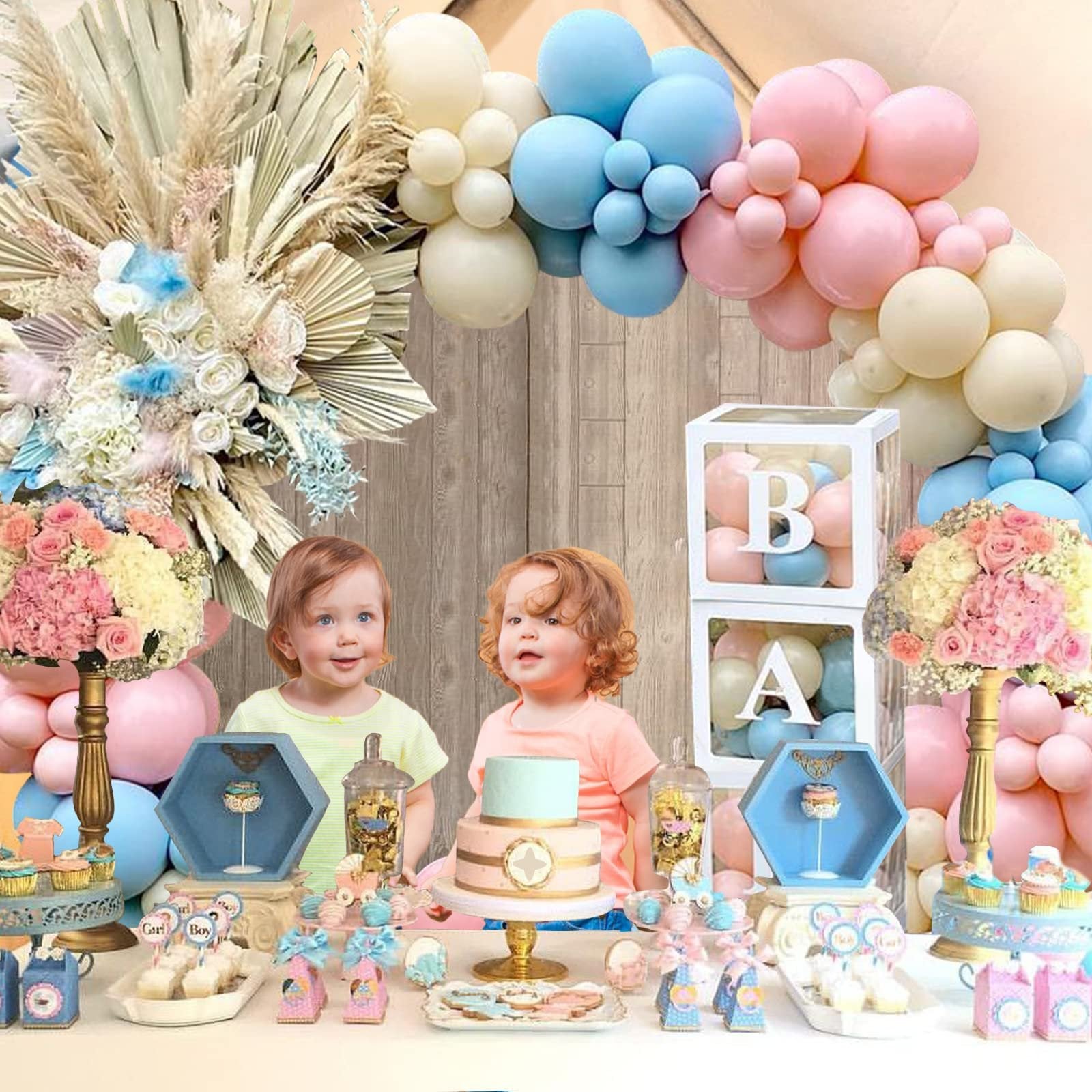 Two babies at a gender reveal party table with pink and blue balloons, cake, and decorations.