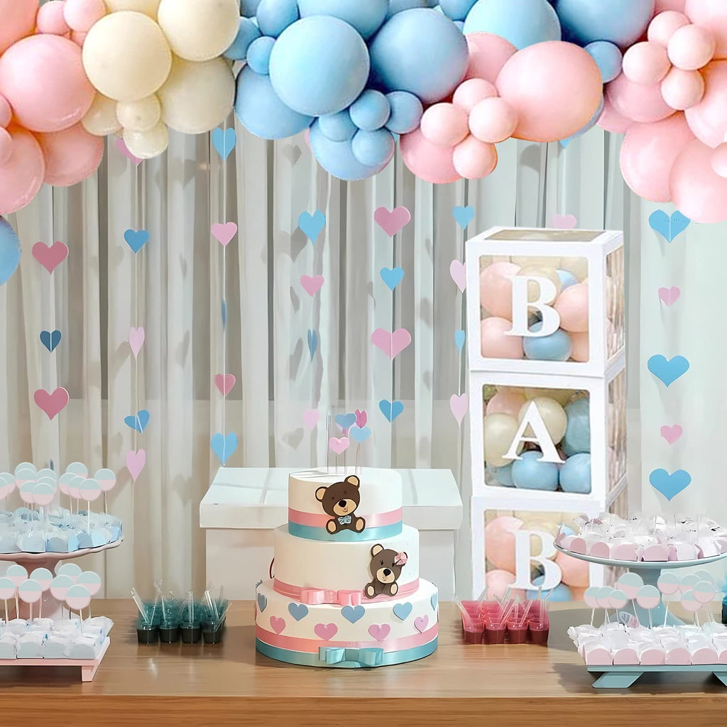 Gender reveal party table with a tiered cake, balloon arch, and decorative boxes spelling 'BABY'.