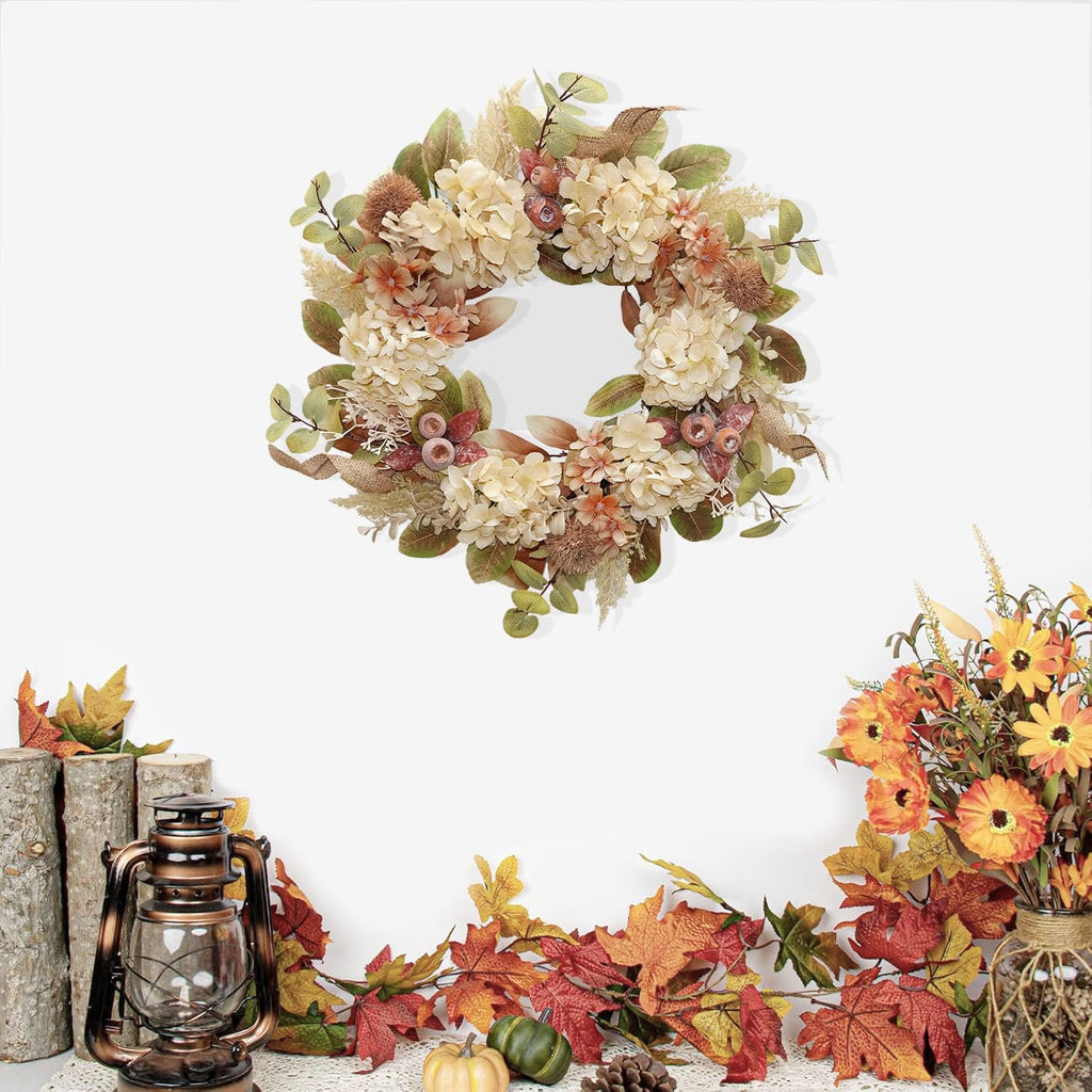 Fall wreath with faux hydrangea, pampas grass, burlap, and flowers, arranged with autumn leaves, a lantern, and logs.