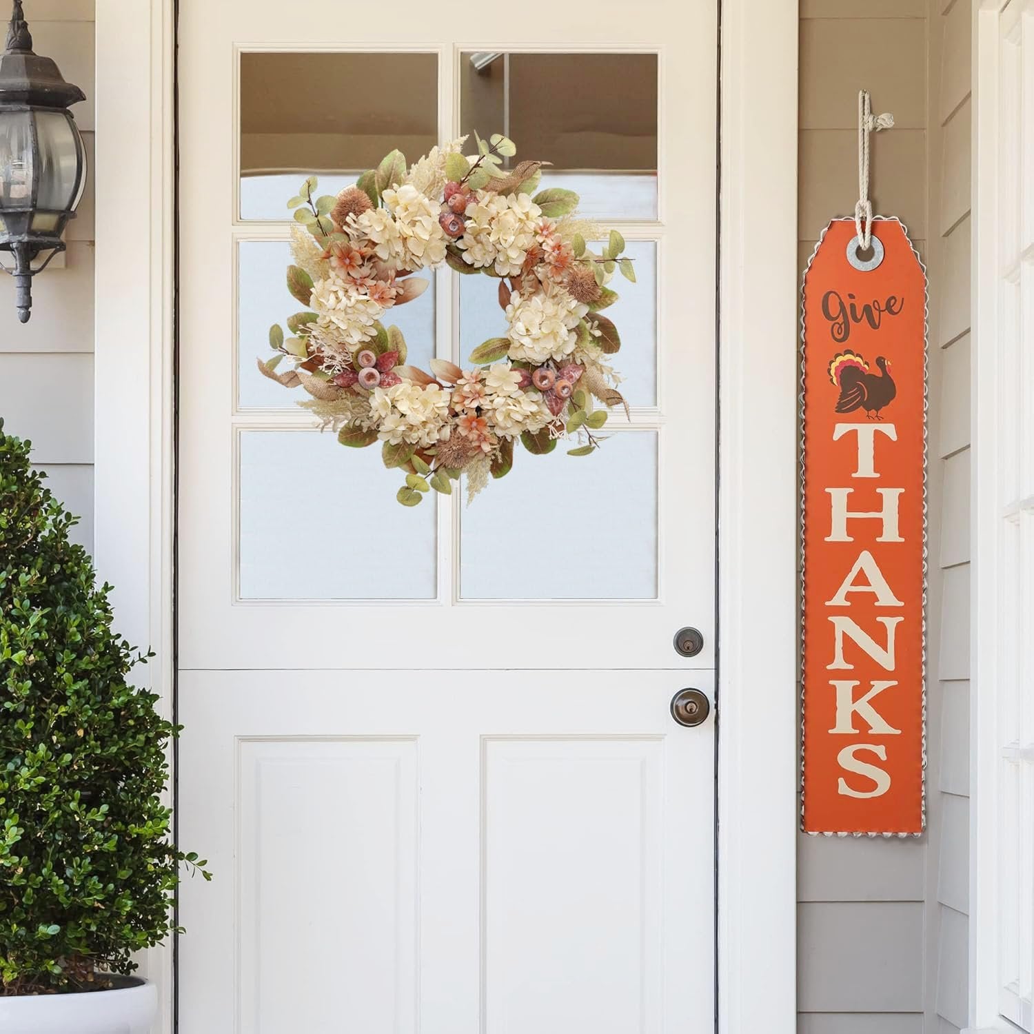 Fall wreath with hydrangeas and pampas grass hanging on a white door next to a 'Give Thanks' sign with a turkey.