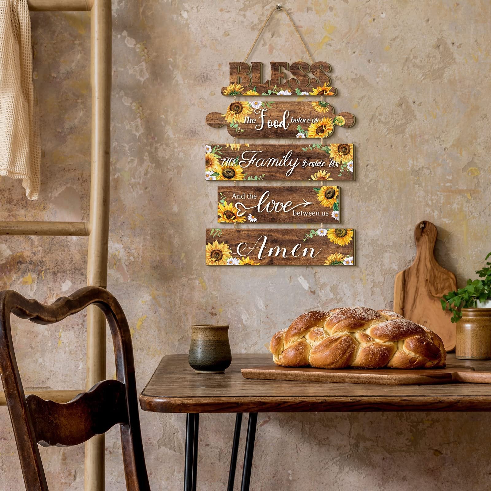 Wooden sunflower kitchen wall sign with five hanging plaques reading 'Bless the food before us, the family beside us, and the love between us, Amen'.