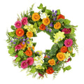 Artificial daisy wreath with green leaves, pink, orange, yellow, and white flowers on a white background.