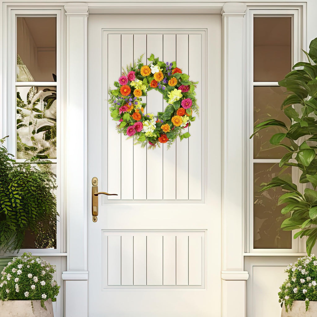 Artificial daisy and gerbera wreath with green leaves hanging on a white paneled door.