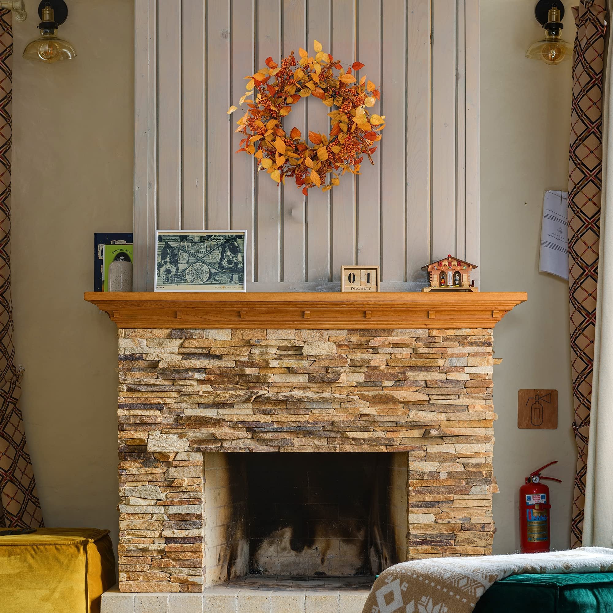 Artificial fall wreath with orange and yellow leaves and berries hanging above a stone fireplace.