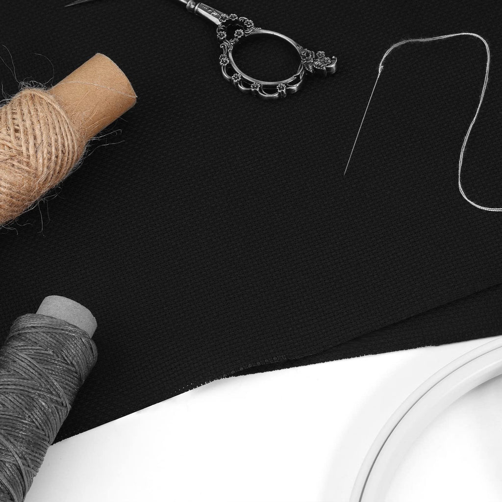 Black Aida cloth cross stitch fabric with sewing supplies including thread, needle, and scissors