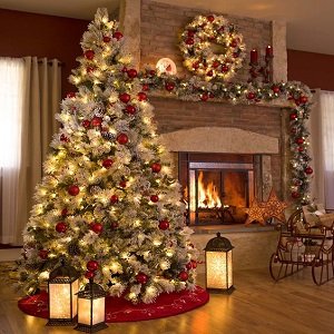 Decorated Christmas tree with warm white string lights and red ornaments next to a fireplace with a wreath and garland.