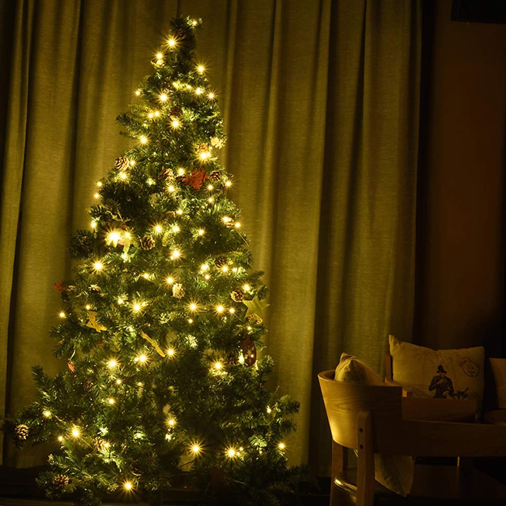 Decorated Christmas tree with warm white LED string lights and pinecones, set against a curtain backdrop.