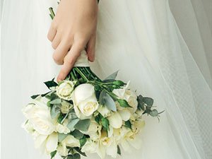 Hand holding a white rose bouquet with eucalyptus leaves, against a white wedding dress.