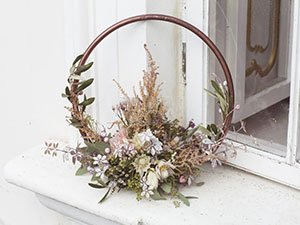 Circular floral arrangement with dried flowers and greenery on a white ledge.