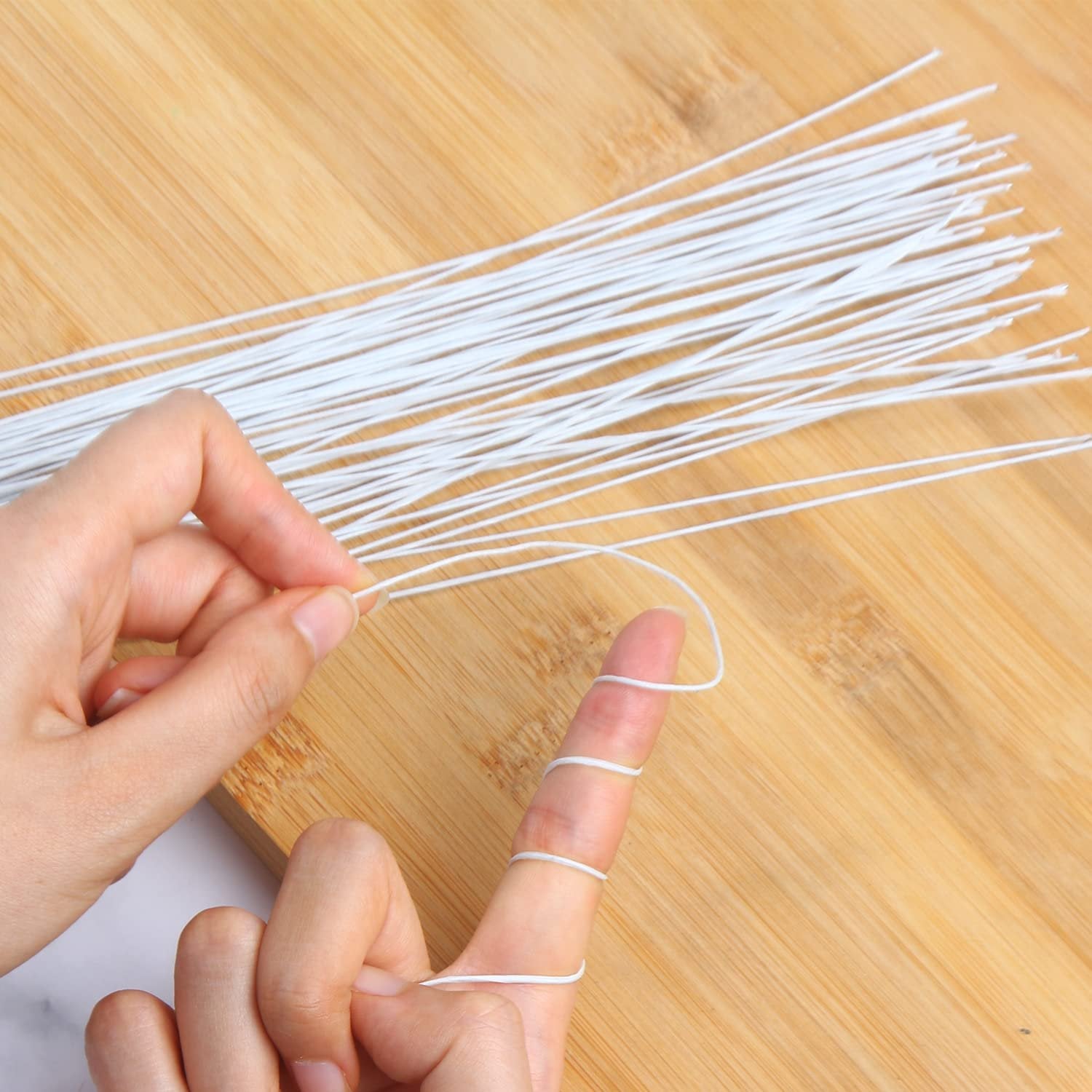 Hands demonstrating how to wrap white floral stem wire around a finger on a wooden surface.