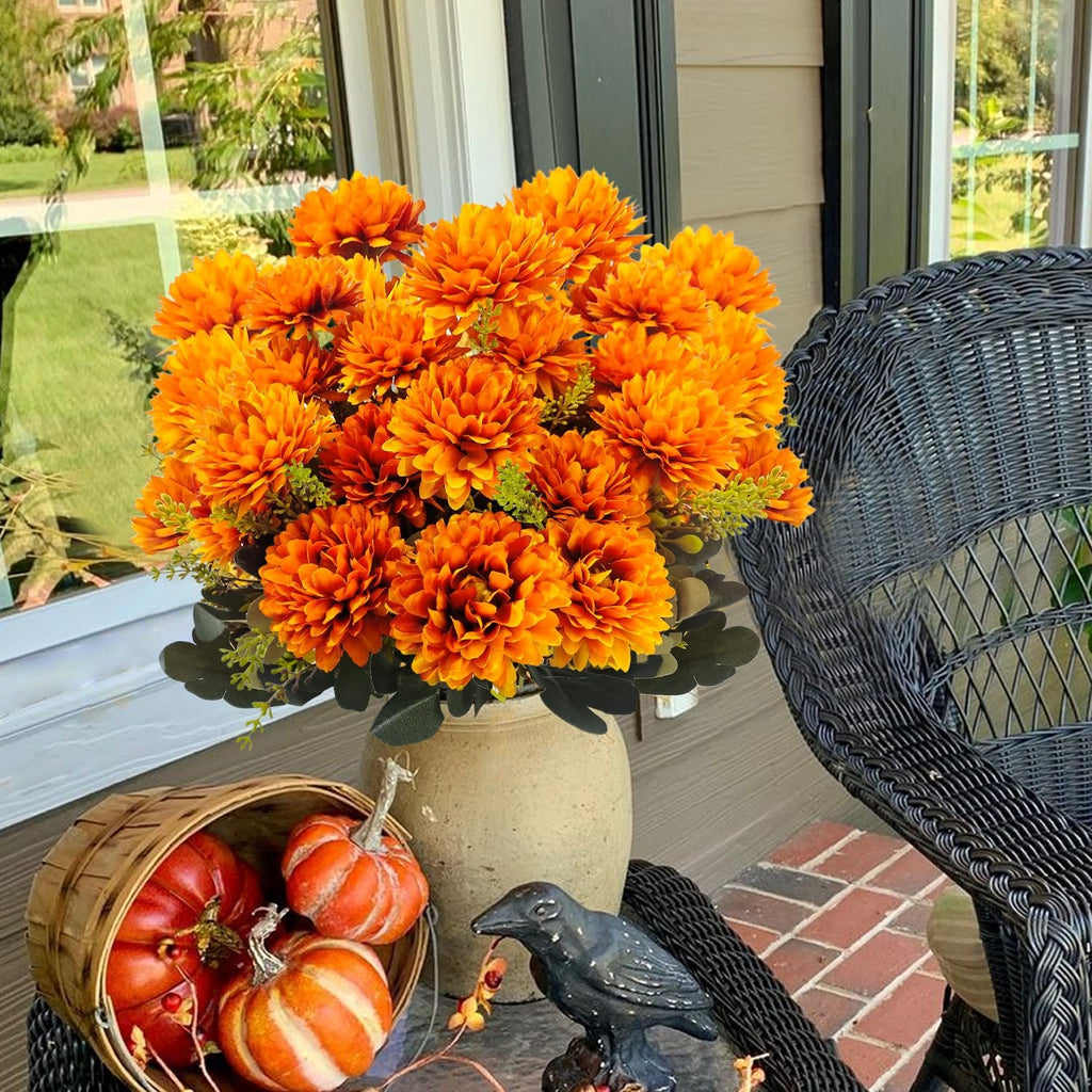 Artificial orange mum bouquet in a vase with pumpkins and a crow figurine on a porch.