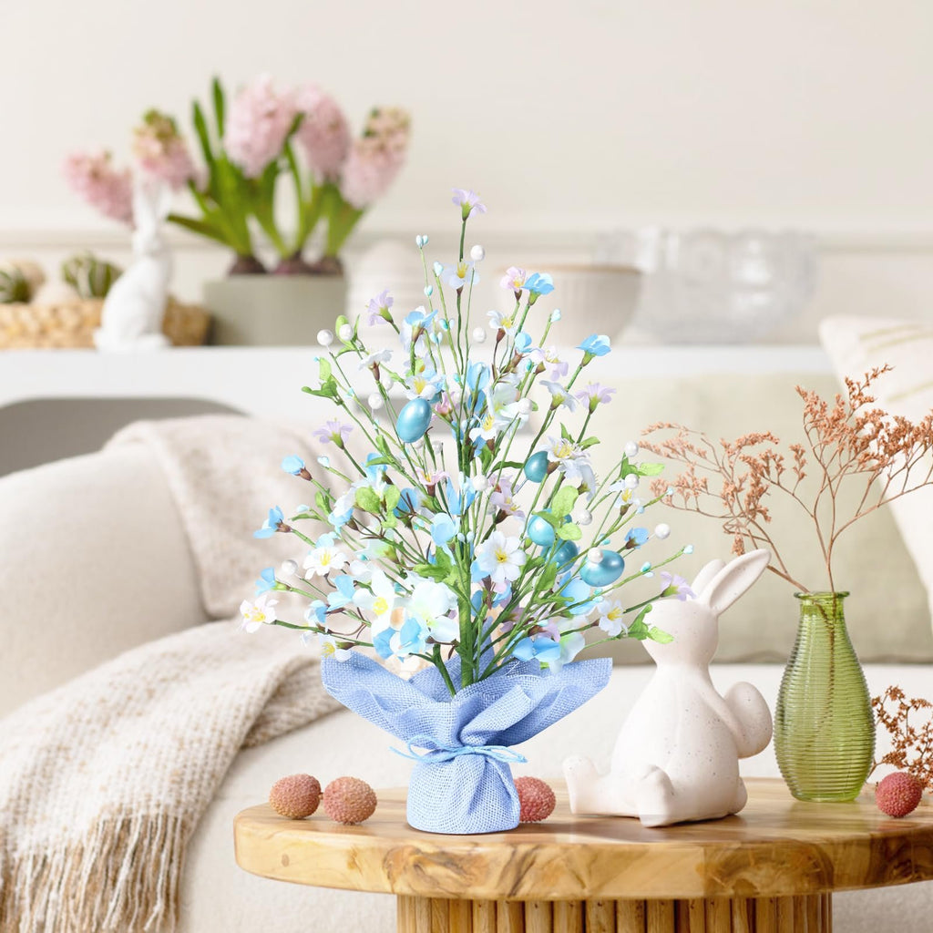 Artificial Easter egg tree with blue eggs and flowers on a wooden table with decorative bunnies and fruit