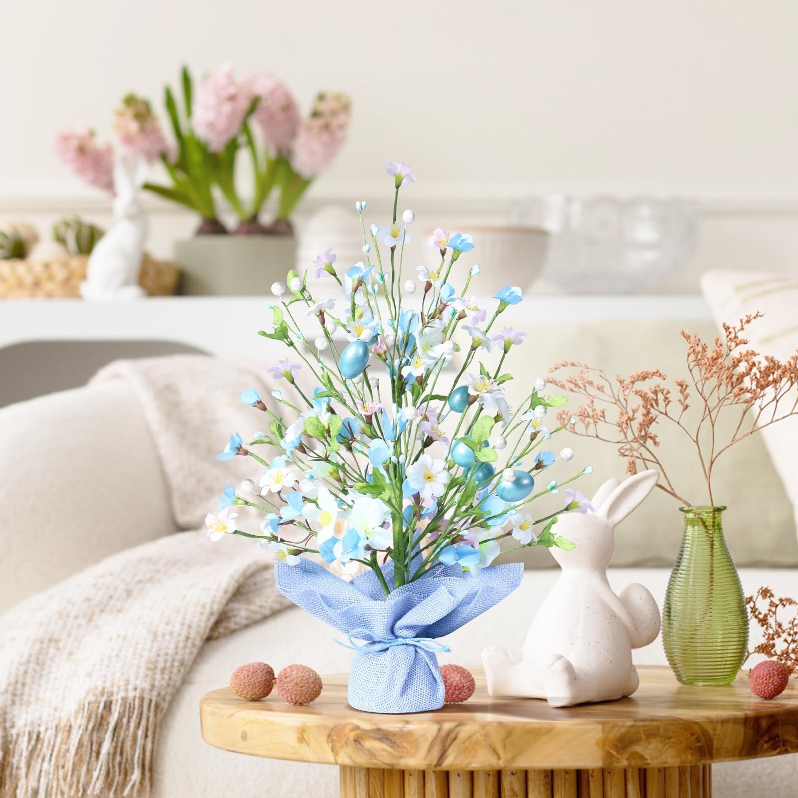 Artificial Easter egg tree with blue eggs and flowers on a wooden table with decorative bunnies and fruit
