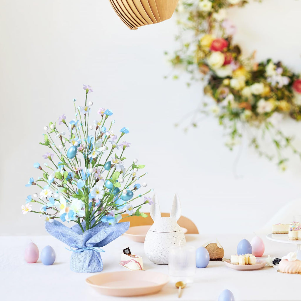 Artificial Easter egg tree with blue eggs, flowers, and pearls on a table with Easter decor.