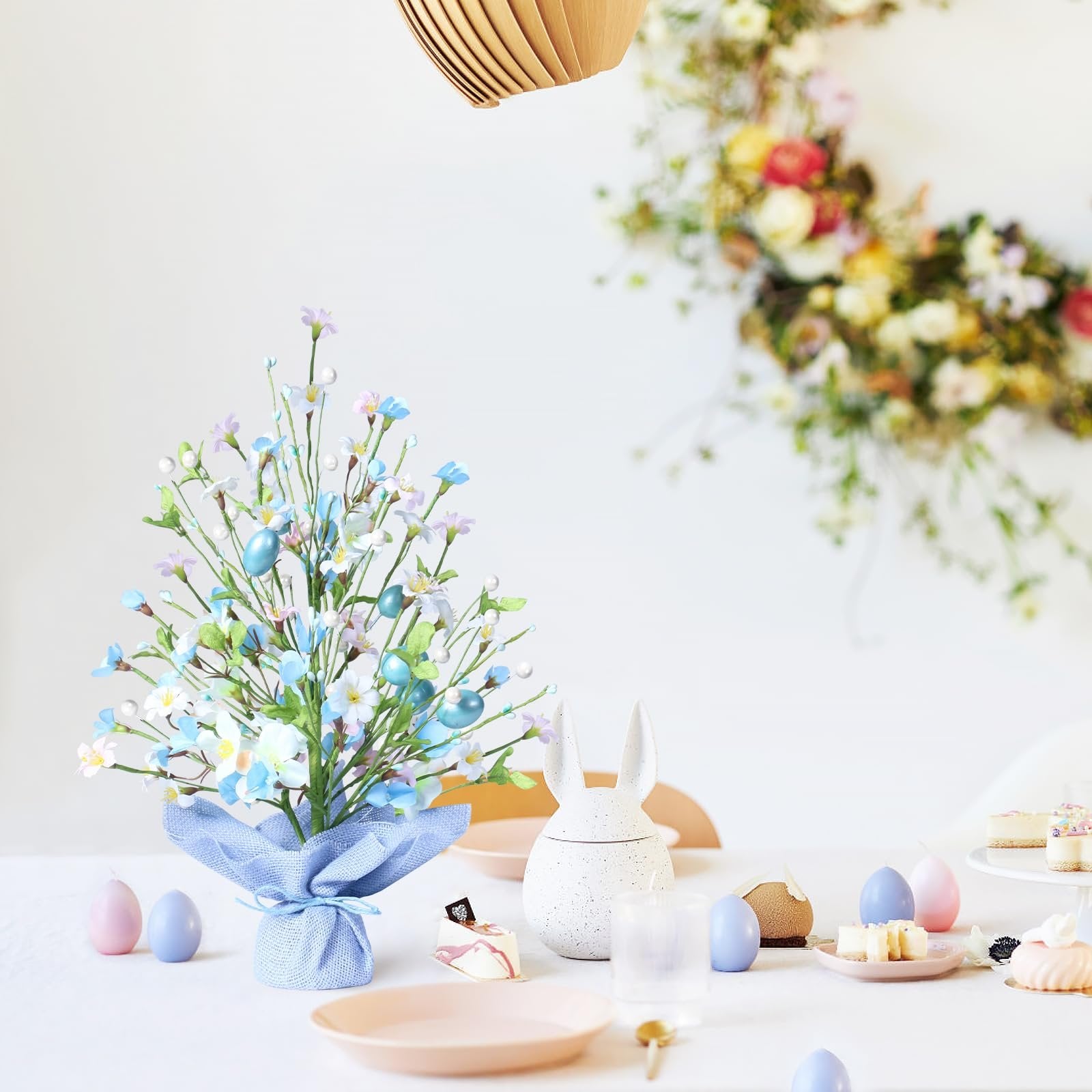 Artificial Easter egg tree with blue eggs, flowers, and pearls on a table with Easter decor.