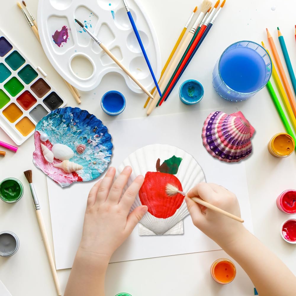 Child's hands painting a large scallop shell with a red apple design, surrounded by art supplies.
