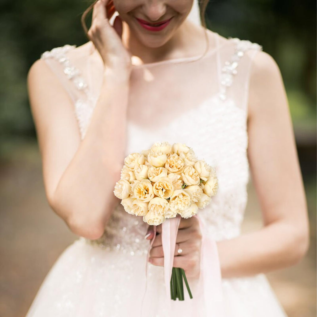 Bride holding a bouquet of champagne artificial peonies and ranunculus flowers with pink ribbon