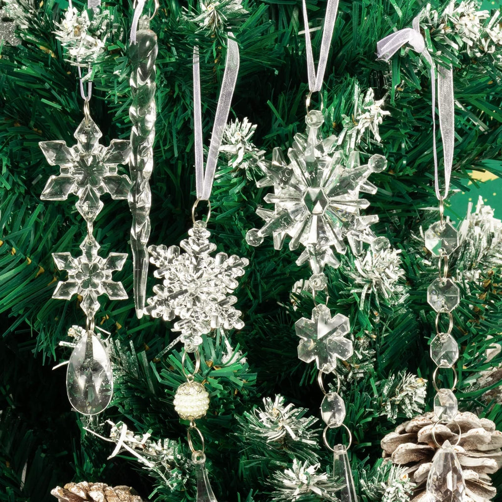 Close-up of clear acrylic Christmas tree ornaments including snowflakes, icicles, and beaded garlands hanging on a green artificial tree.