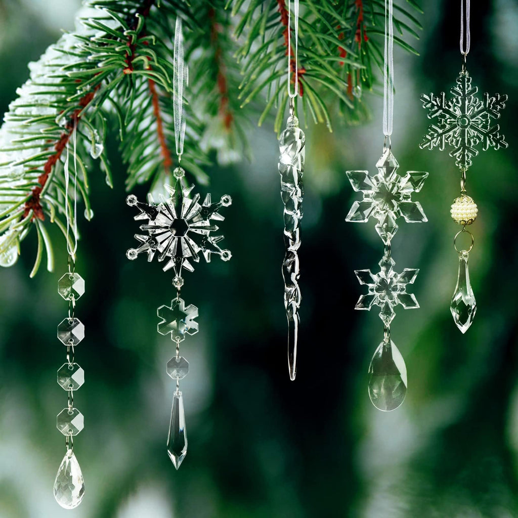 Clear acrylic Christmas ornaments including snowflakes, icicles, and beaded garlands hanging from a frosted pine branch.