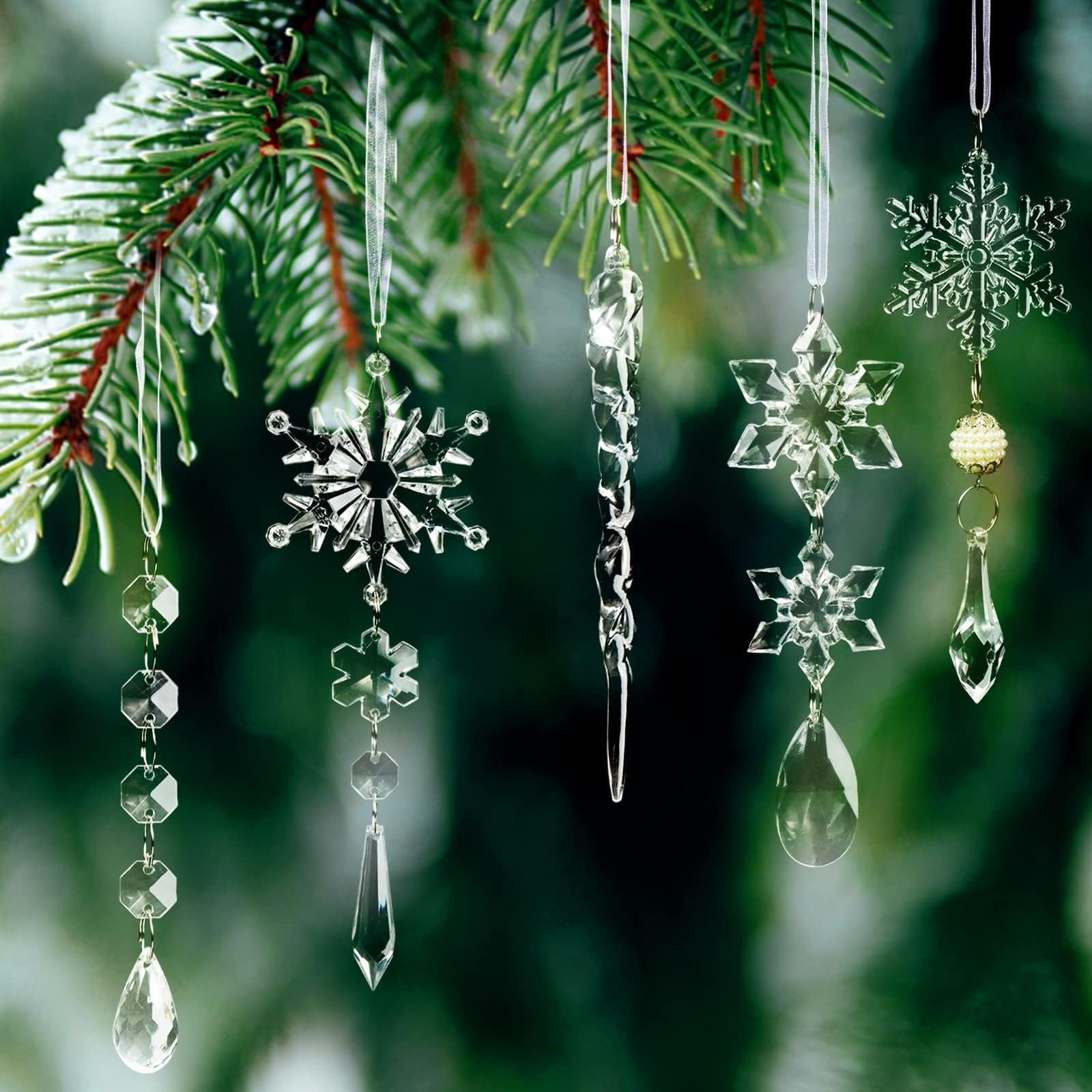 Clear acrylic Christmas ornaments including snowflakes, icicles, and beaded garlands hanging from a frosted pine branch.