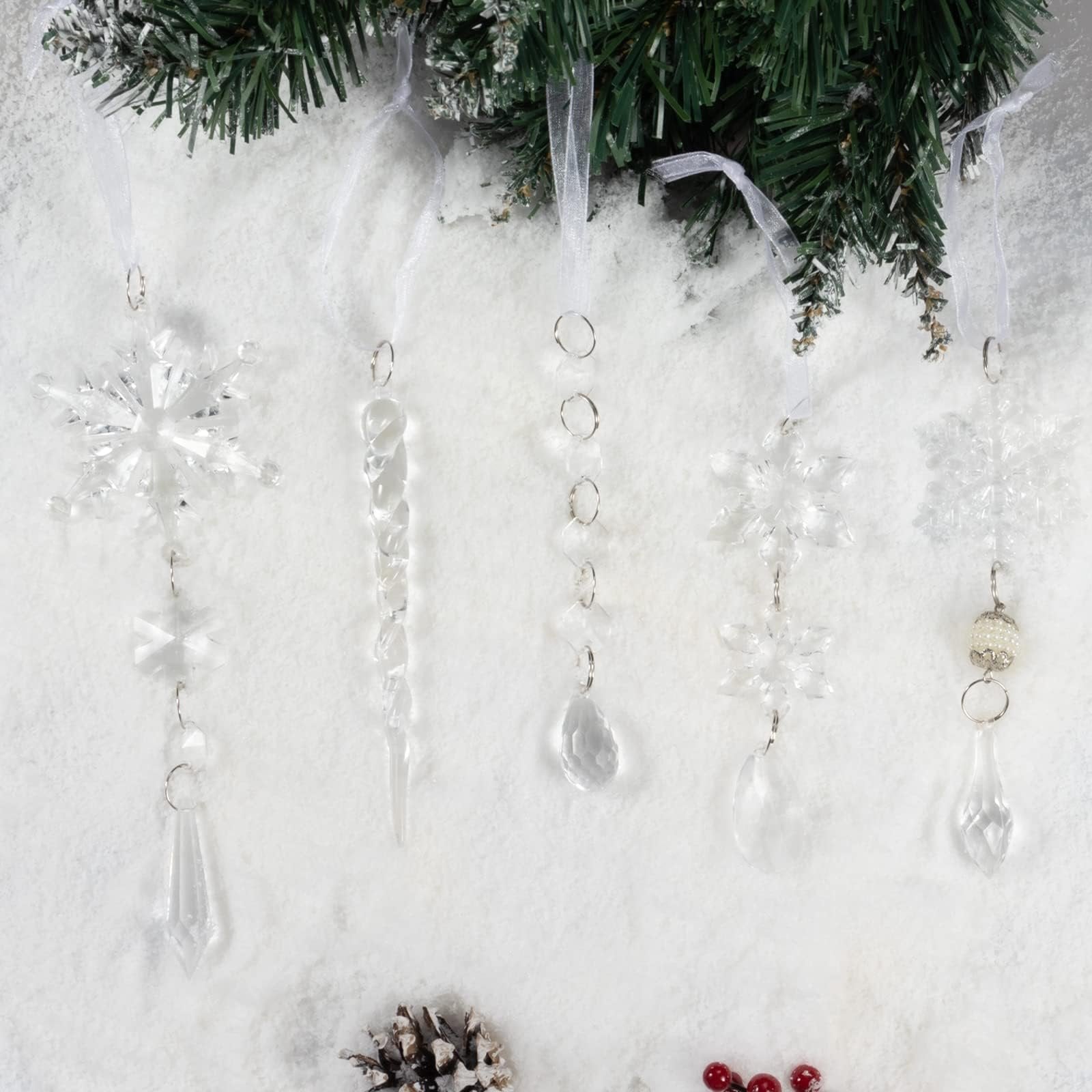 Clear acrylic Christmas ornaments including snowflakes and icicles hanging from a pine branch over a snowy background.