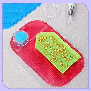 Diamond painting tools including a pink tray with a blue container and green tray of beads, plus a pen with a white tip.