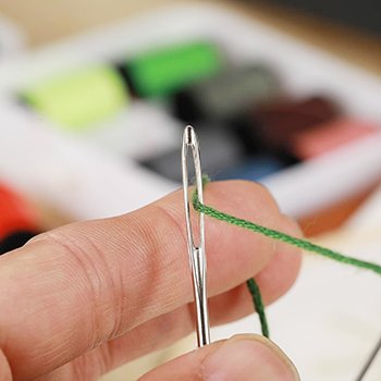 Close-up of a hand threading green yarn through the eye of a large-eye sewing needle.