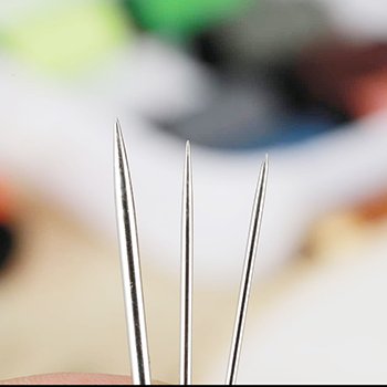 Close-up of three large-eye sewing needles with varying points, showing stainless steel material.