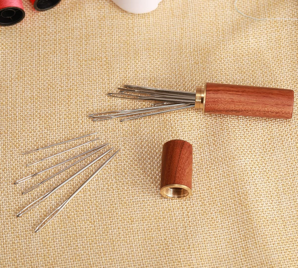 Large-eye sewing needles scattered and in a wooden storage tube on a textured surface