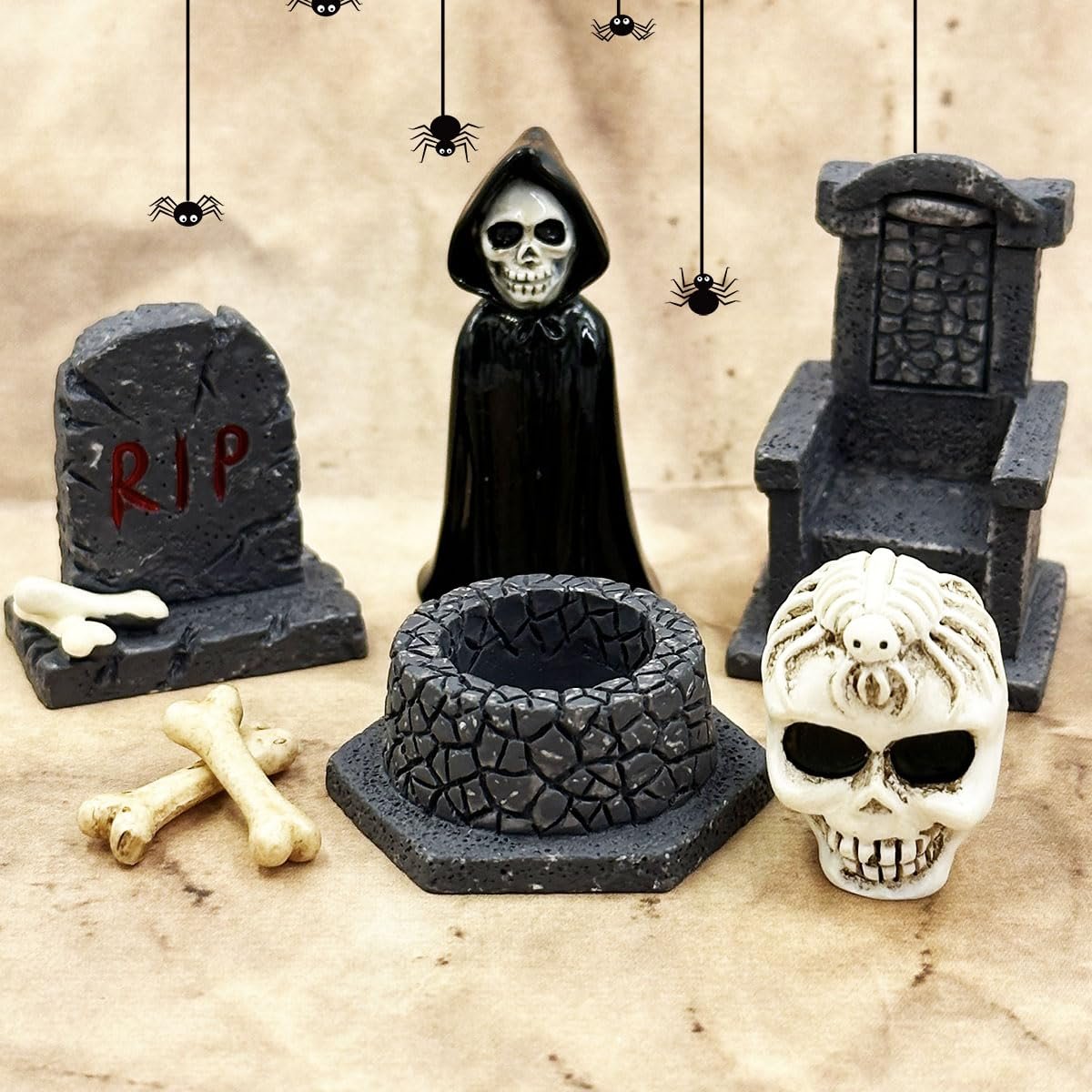 Halloween miniature figurines including a grim reaper, tombstone, skull, and well on a textured background with hanging spiders.