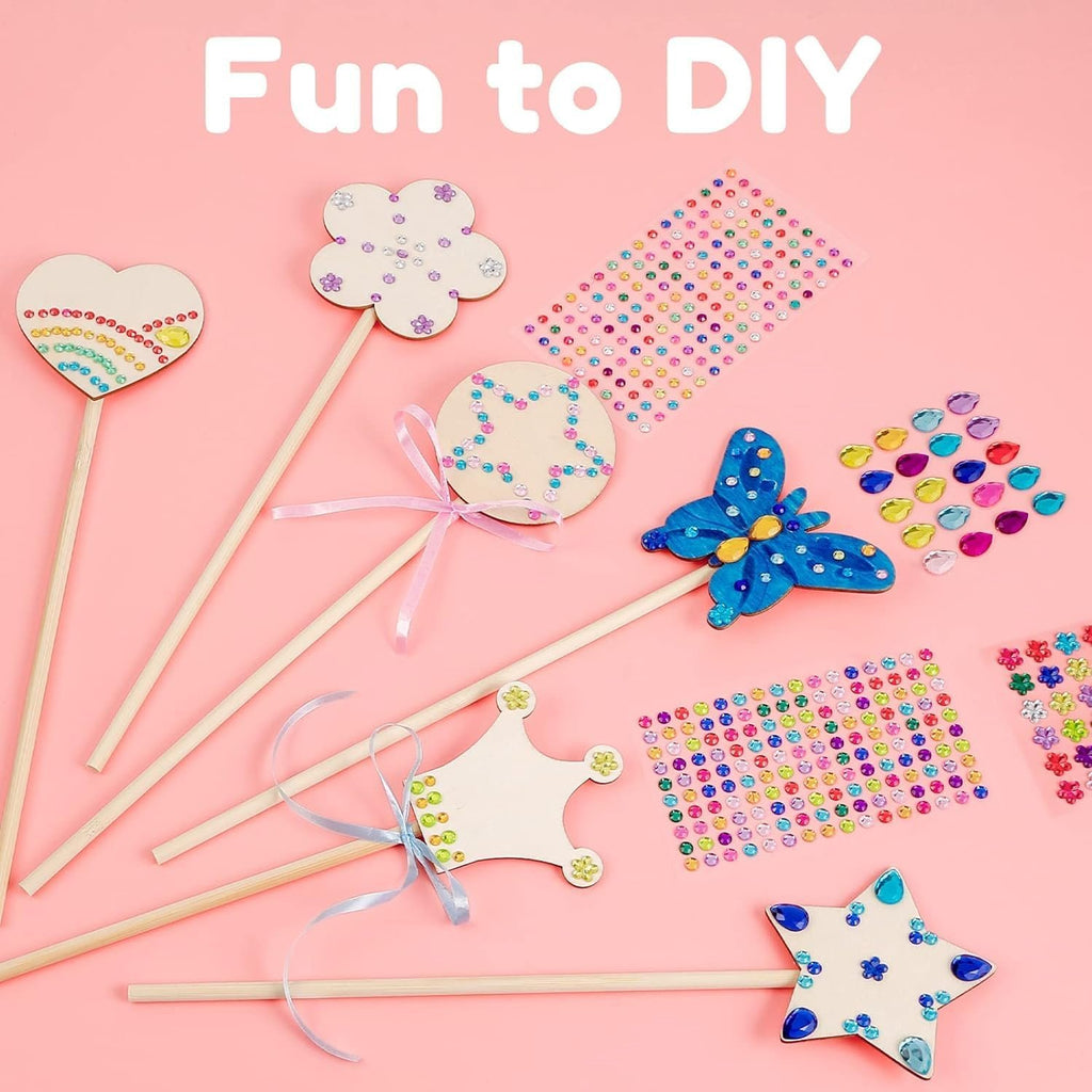 Unfinished wooden fairy wands and craft supplies including gem stickers and ribbons on a pink background