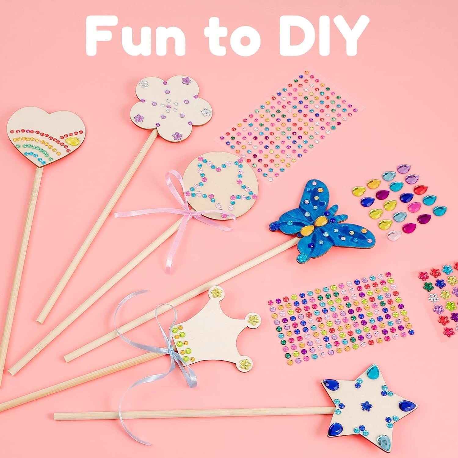 Unfinished wooden fairy wands and craft supplies including gem stickers and ribbons on a pink background