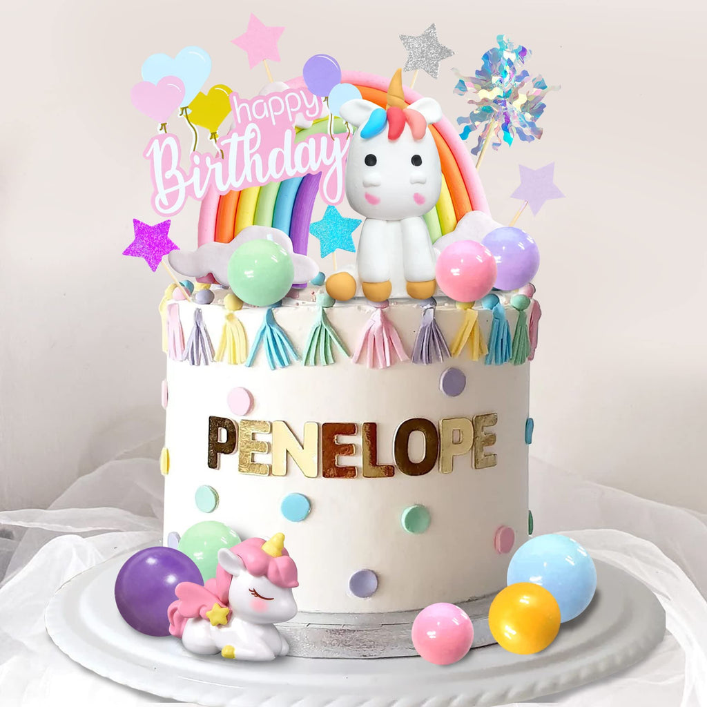 Unicorn rainbow cake topper set with 'Happy Birthday' text and decorative balls on a cake.