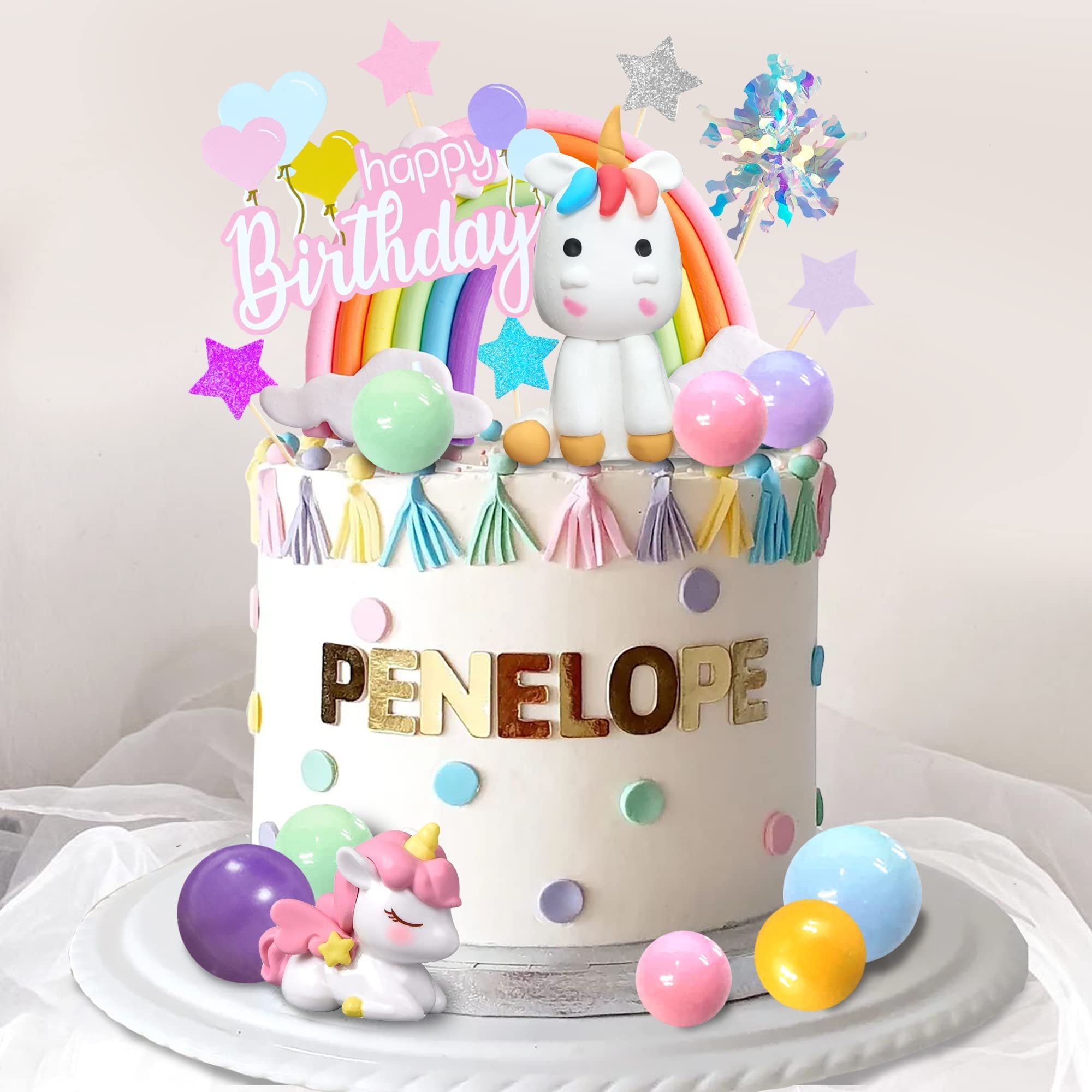 Unicorn rainbow cake topper set with 'Happy Birthday' text and decorative balls on a cake.
