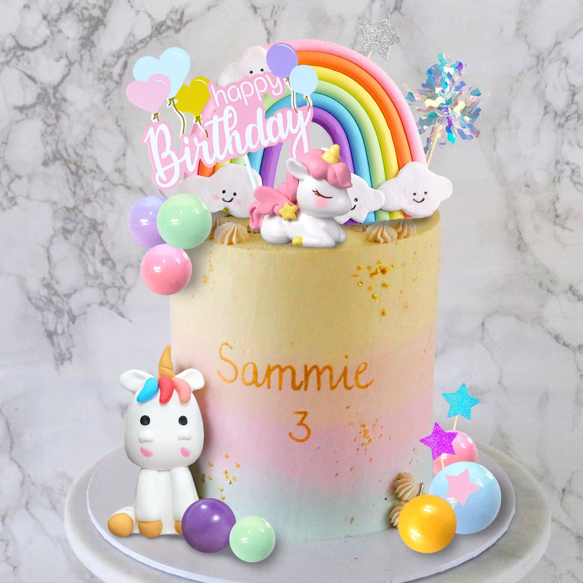 Unicorn rainbow cake topper set with foam balls, foil firework, and paper stars on a decorated cake.
