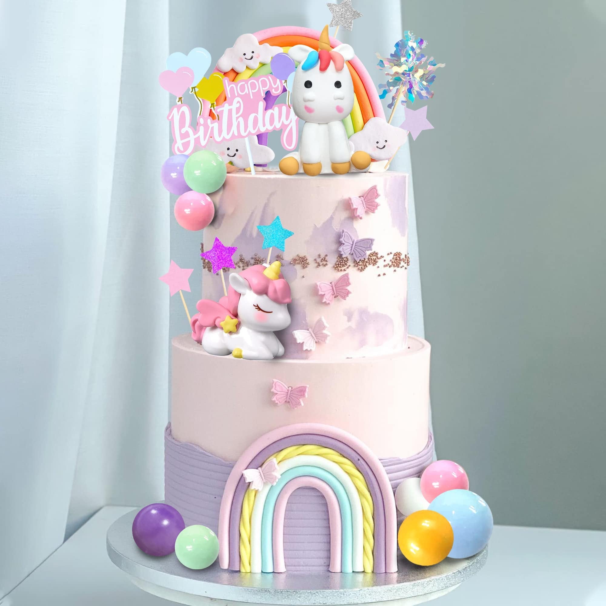Unicorn rainbow cake topper set with happy birthday sign and colorful balloons on a tiered cake.