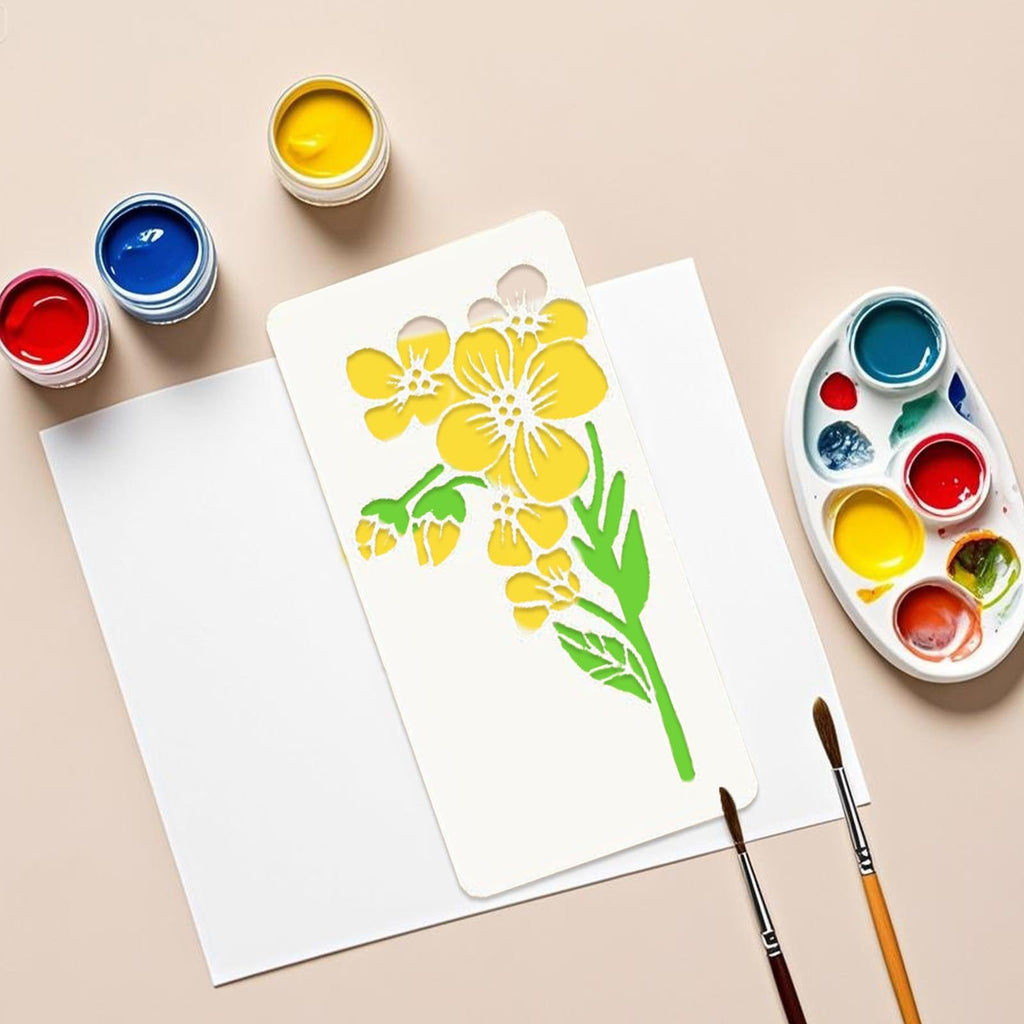 Flower stencil template with yellow flowers and green leaves, next to paints and brushes on paper.