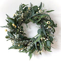 Artificial olive and eucalyptus wreath with white berries and yellow accents on a white background